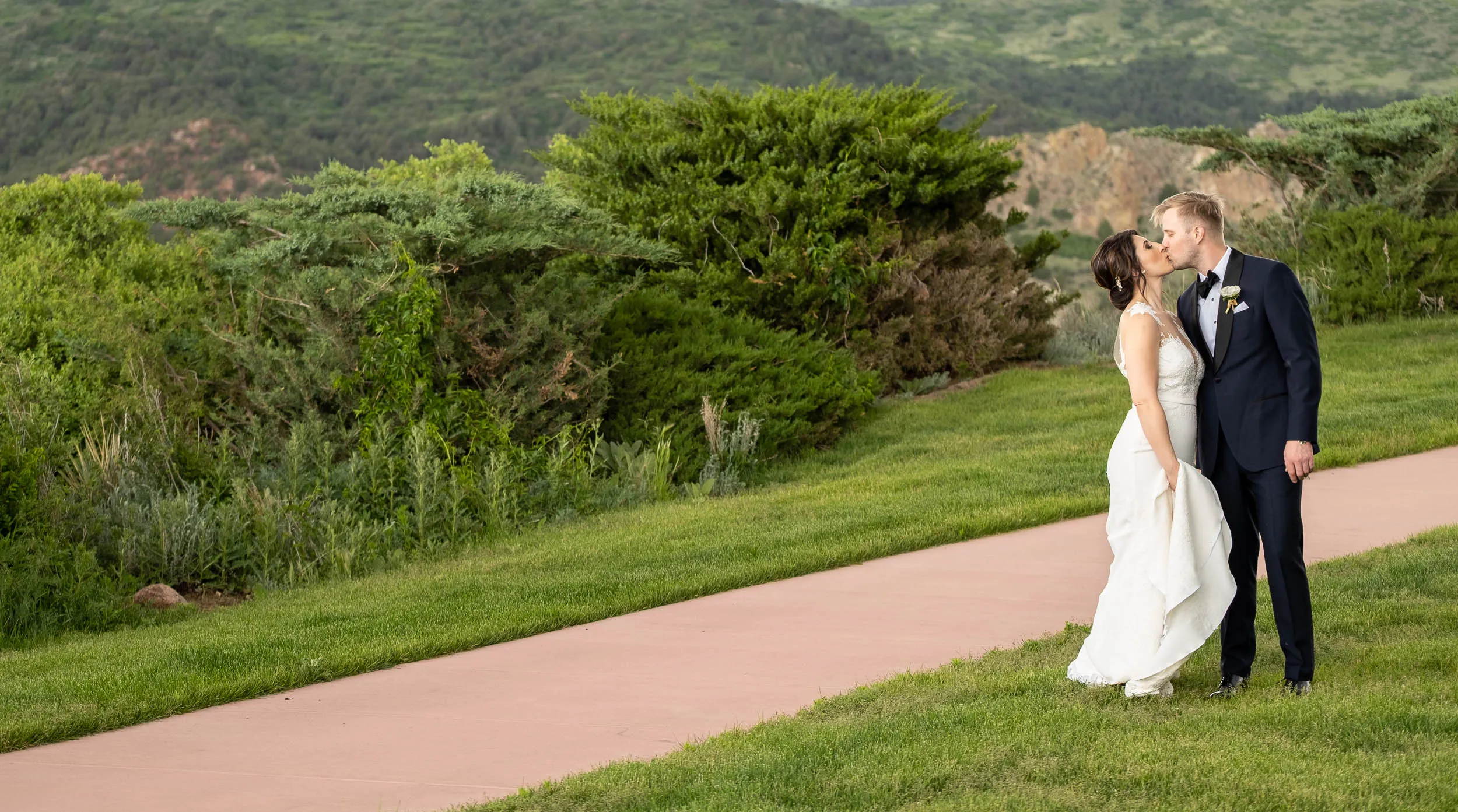 Bride and groom kissing beside a garden path overlooking green hills