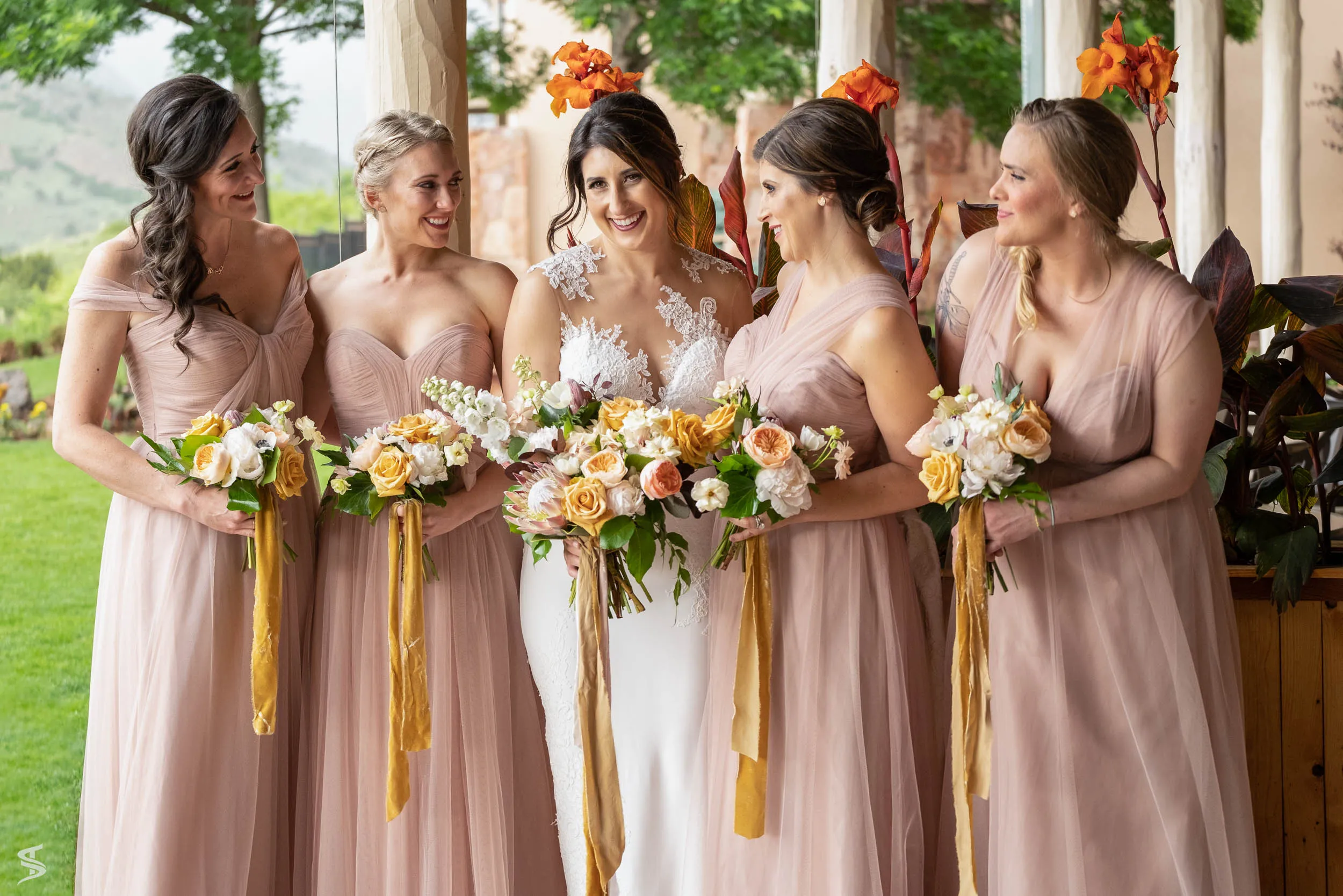 Bride smiling with four bridesmaids in blush dresses, holding colorful bouquets at Garden of the Gods, Colorado.