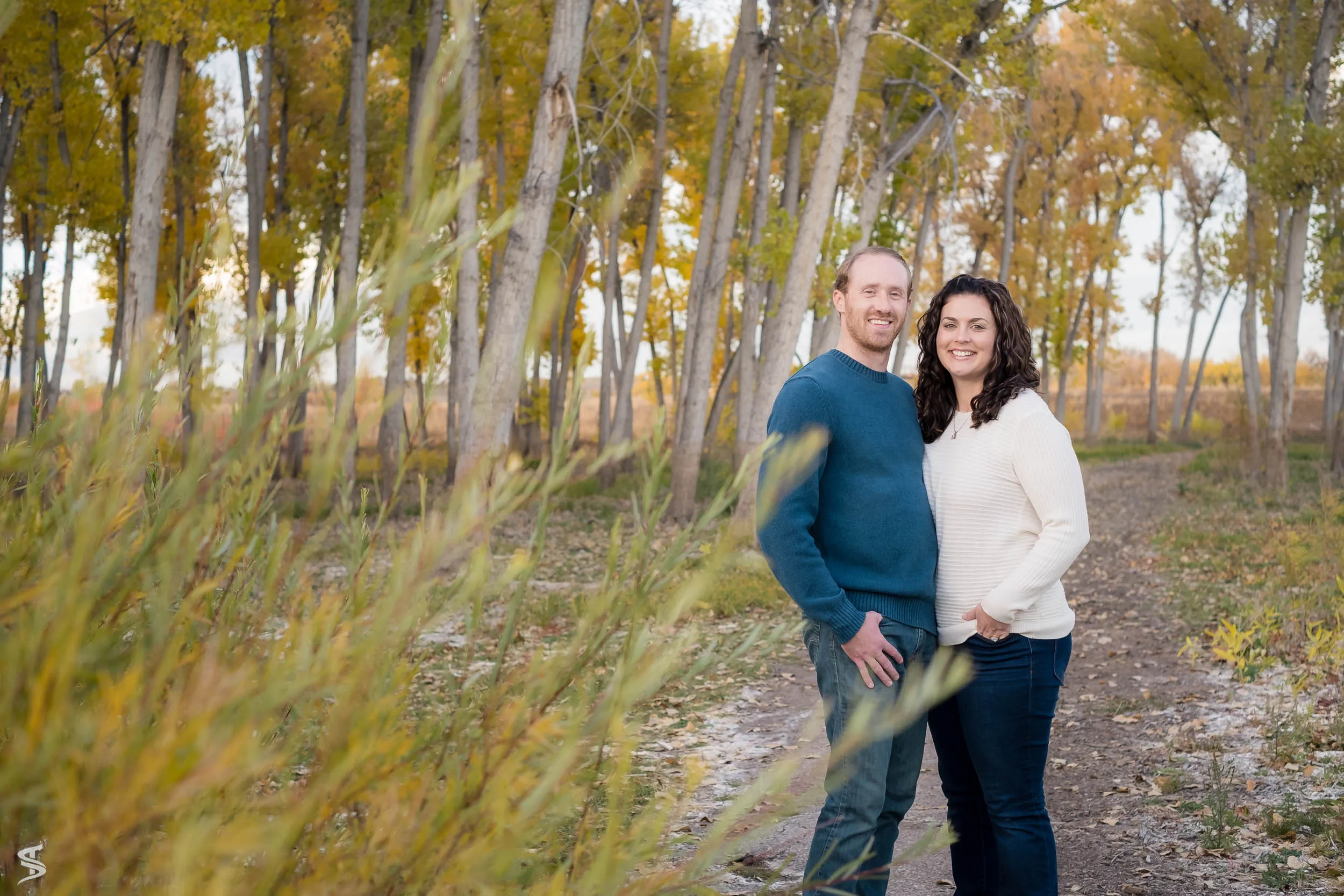Couple standing close together on a woodland path surrounded by autumn trees.