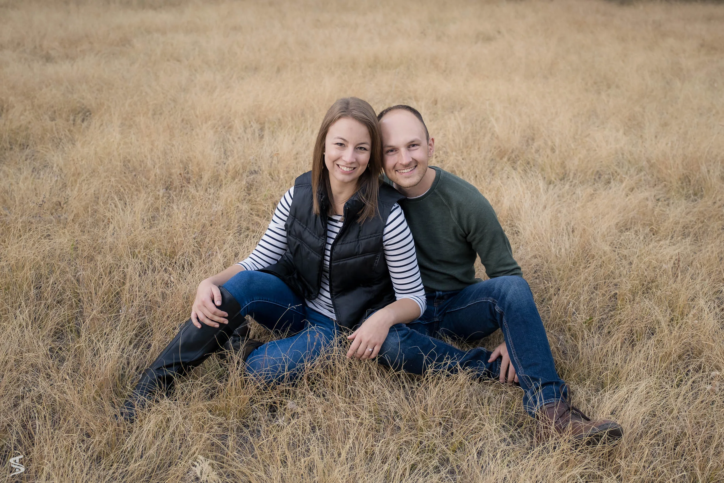Smiling couple sitting close together in a field of golden grass.