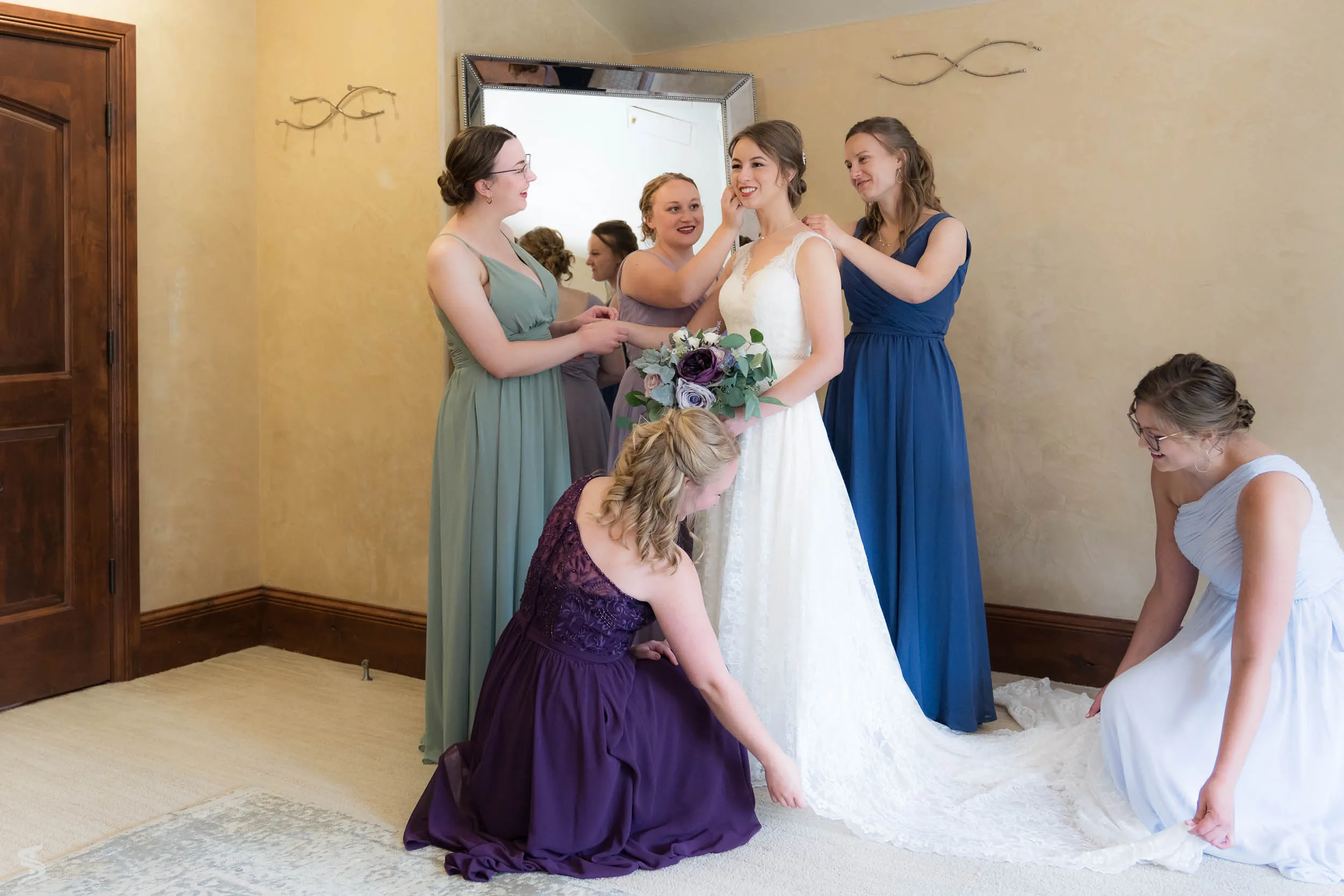 Bride surrounded by attendants helping adjust her dress and train before the wedding.