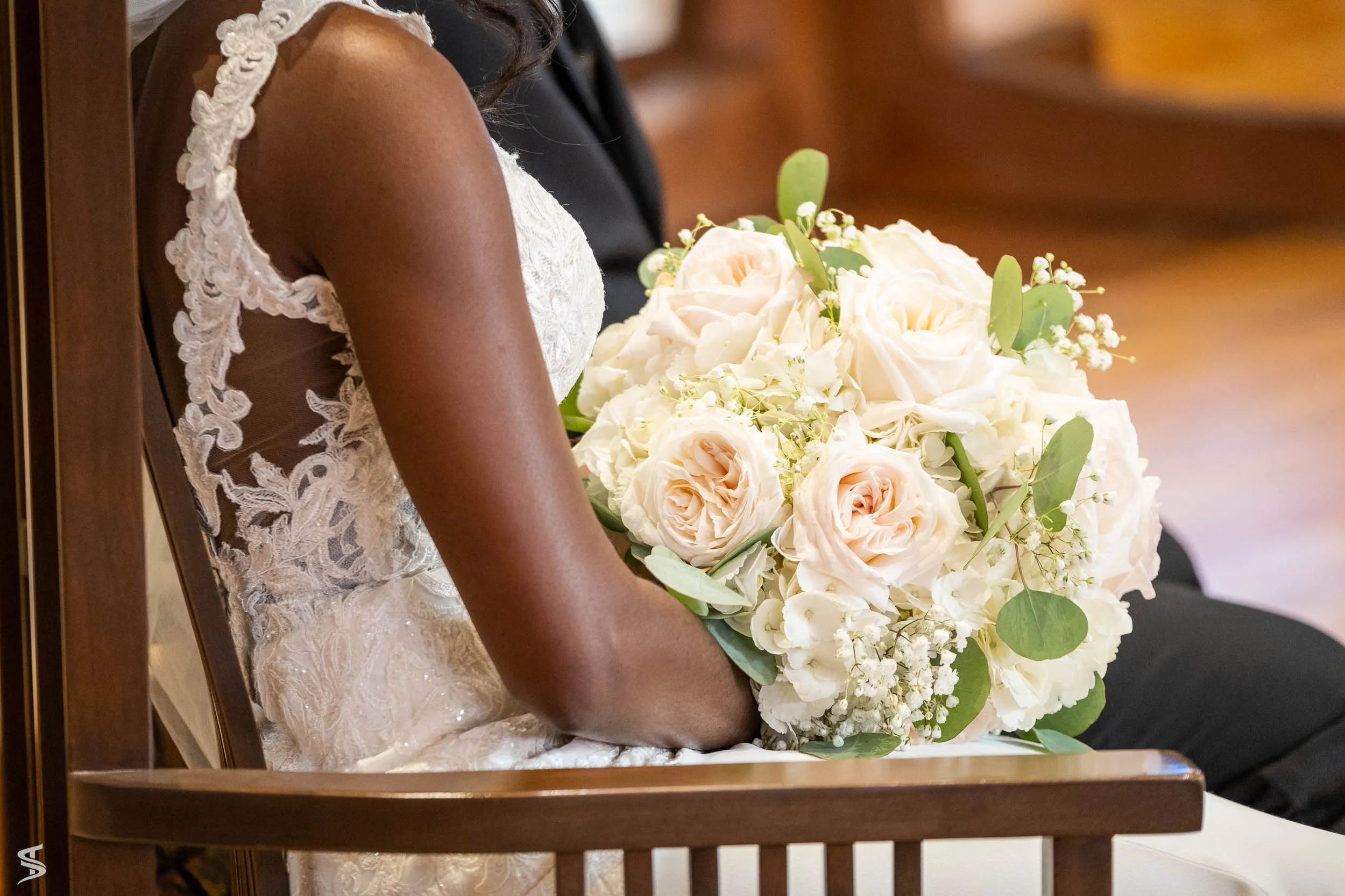 Close-up of a seated bride holding a bouquet of cream and blush roses against her lace wedding dress.