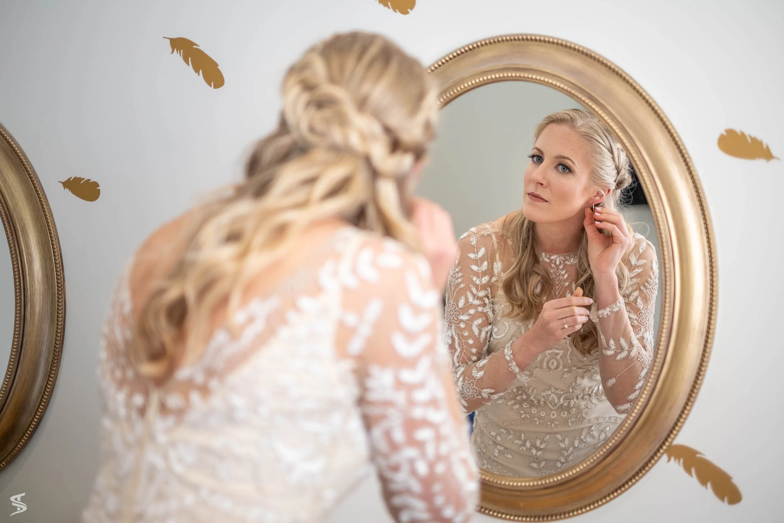 Bride adjusting her earring in an oval mirror while getting ready for her wedding.