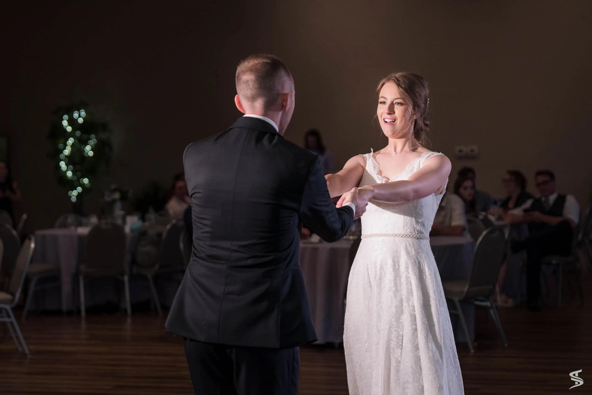 Bride smiling and holding the groom’s hands as they dance across the wedding reception floor.
