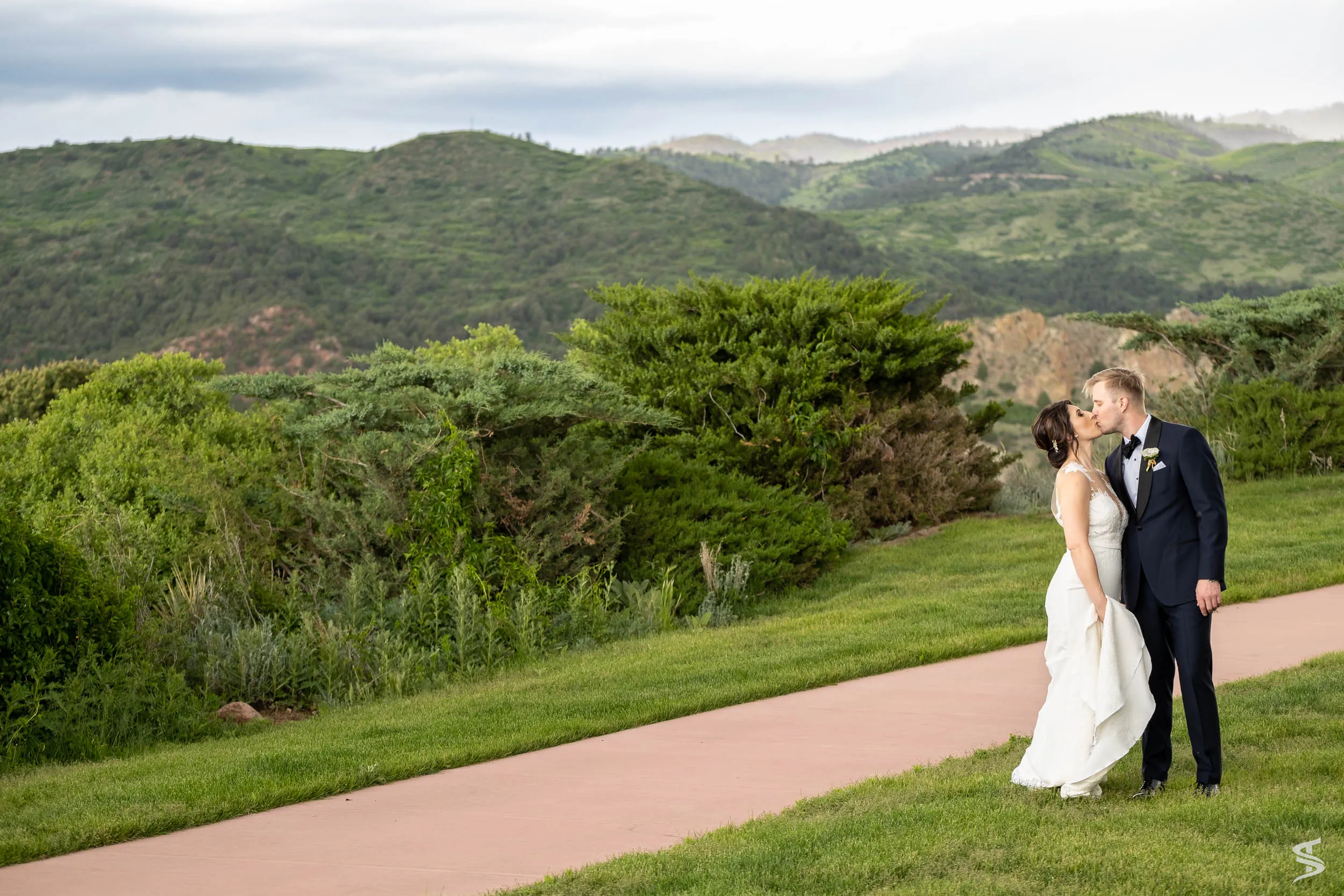 Bride and groom kissing beside a garden path overlooking green hills