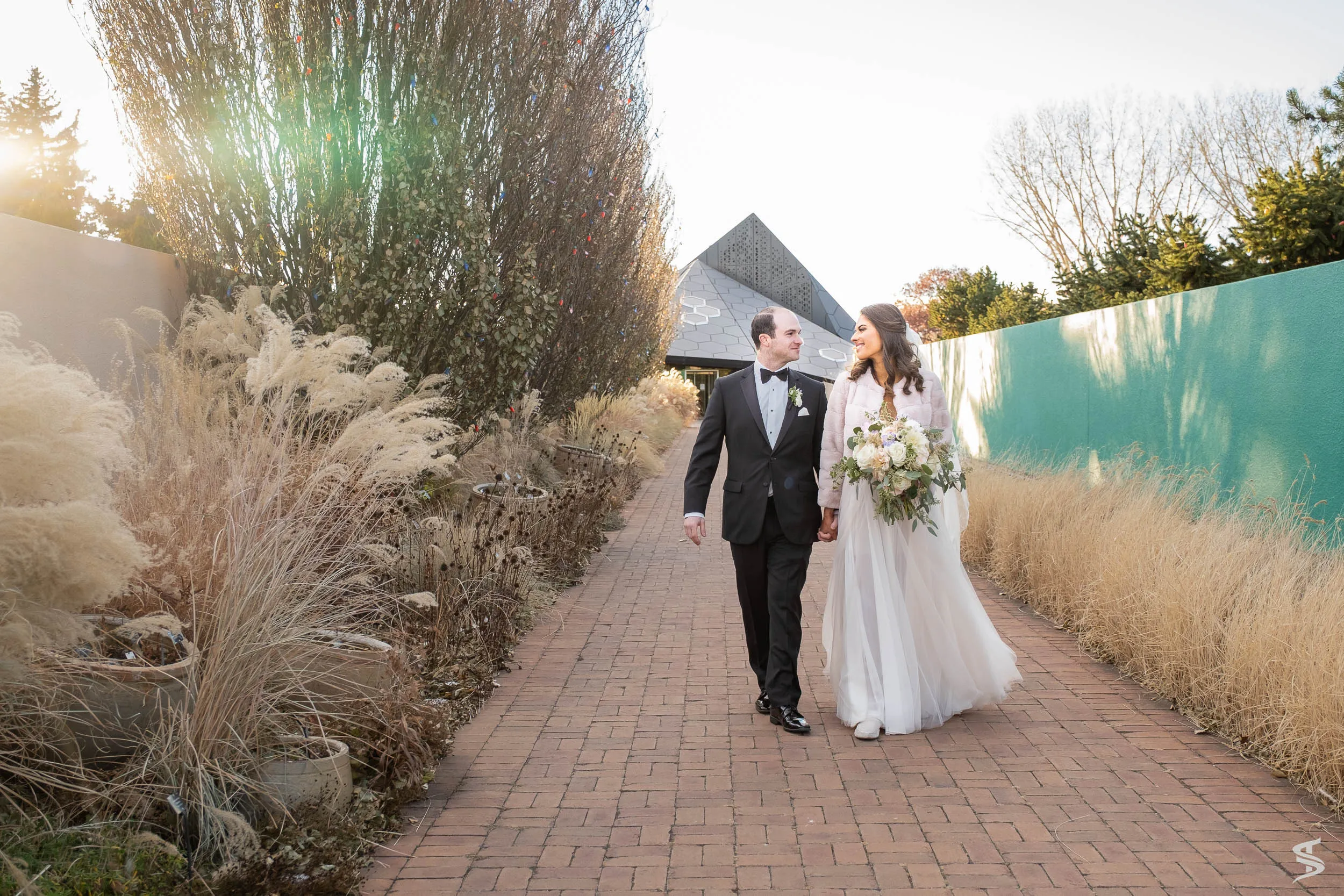 Newlyweds walking hand in hand beside a turquoise wall