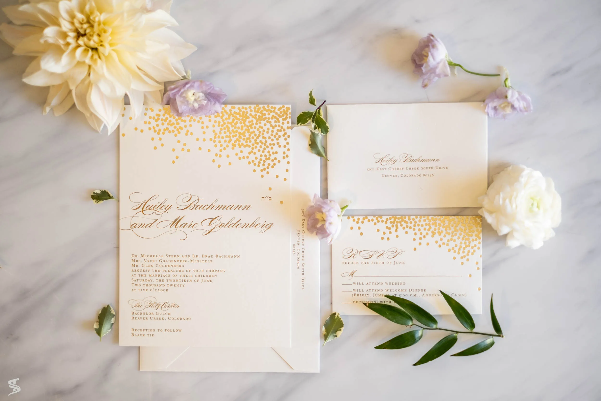 Wedding invitation suite with gold detailing arranged on a marble surface with pale flowers and greenery.
