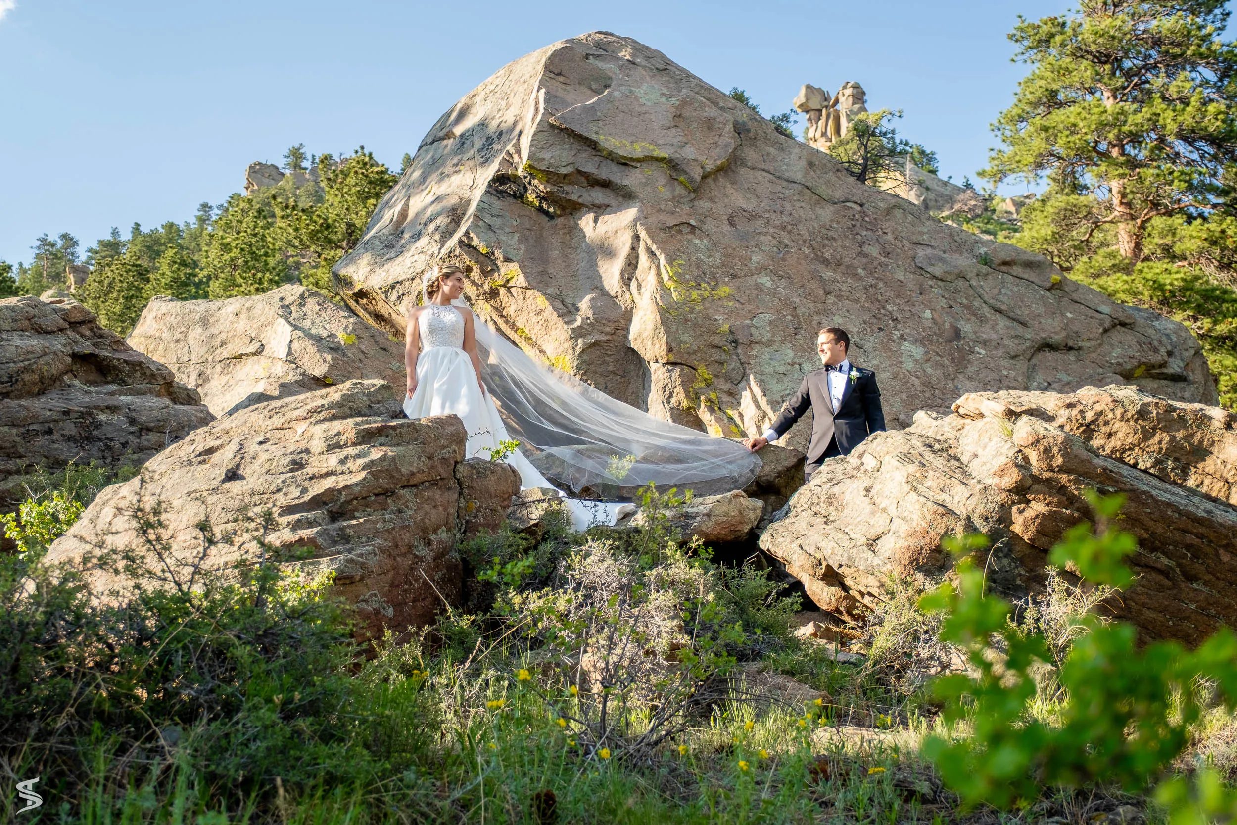 Bride and groom posing among large mountain boulders, with her veil flowing between them.