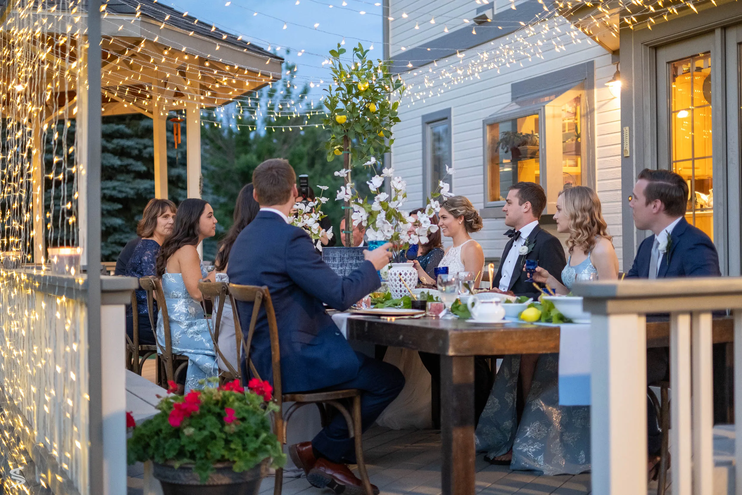 Newlyweds and wedding guests dining beneath string lights
