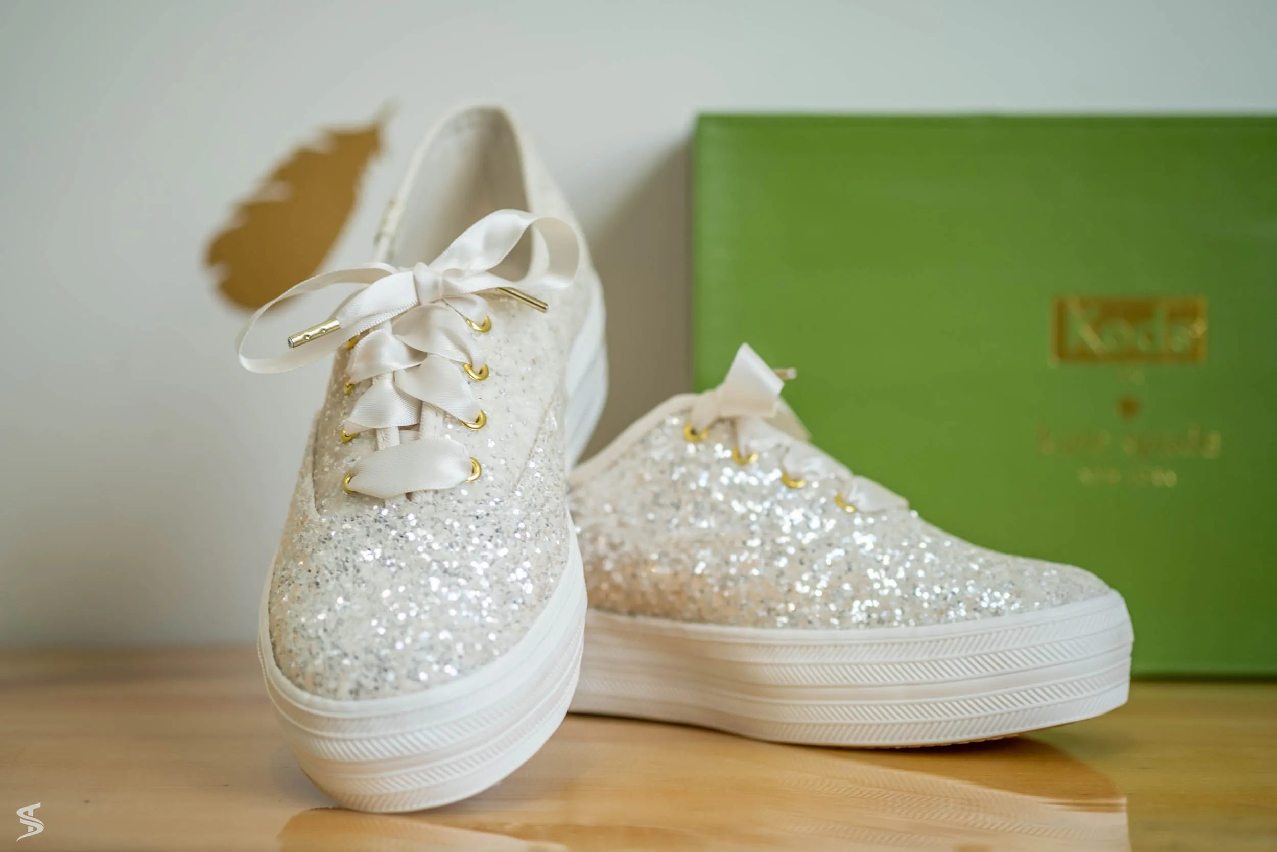 White bridal sneakers decorated with pearls and glitter, displayed beside a green shoebox.
