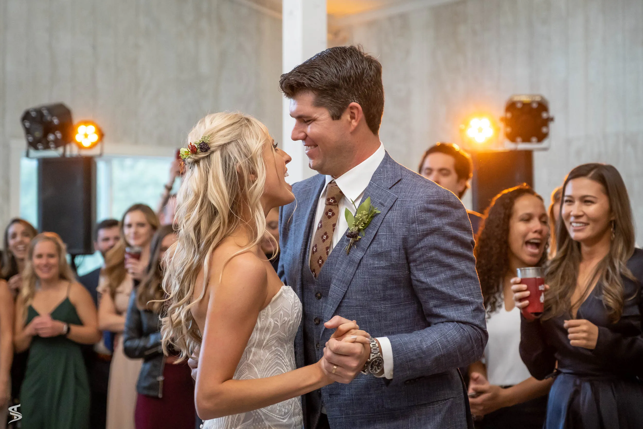 Bride and groom dancing together at their wedding reception as smiling guests watch.