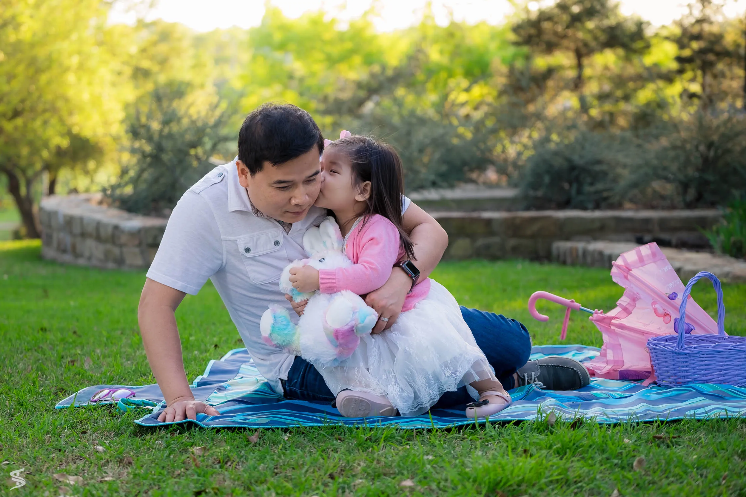Young daughter kissing her father on the cheek while sitting together on a picnic blanket.