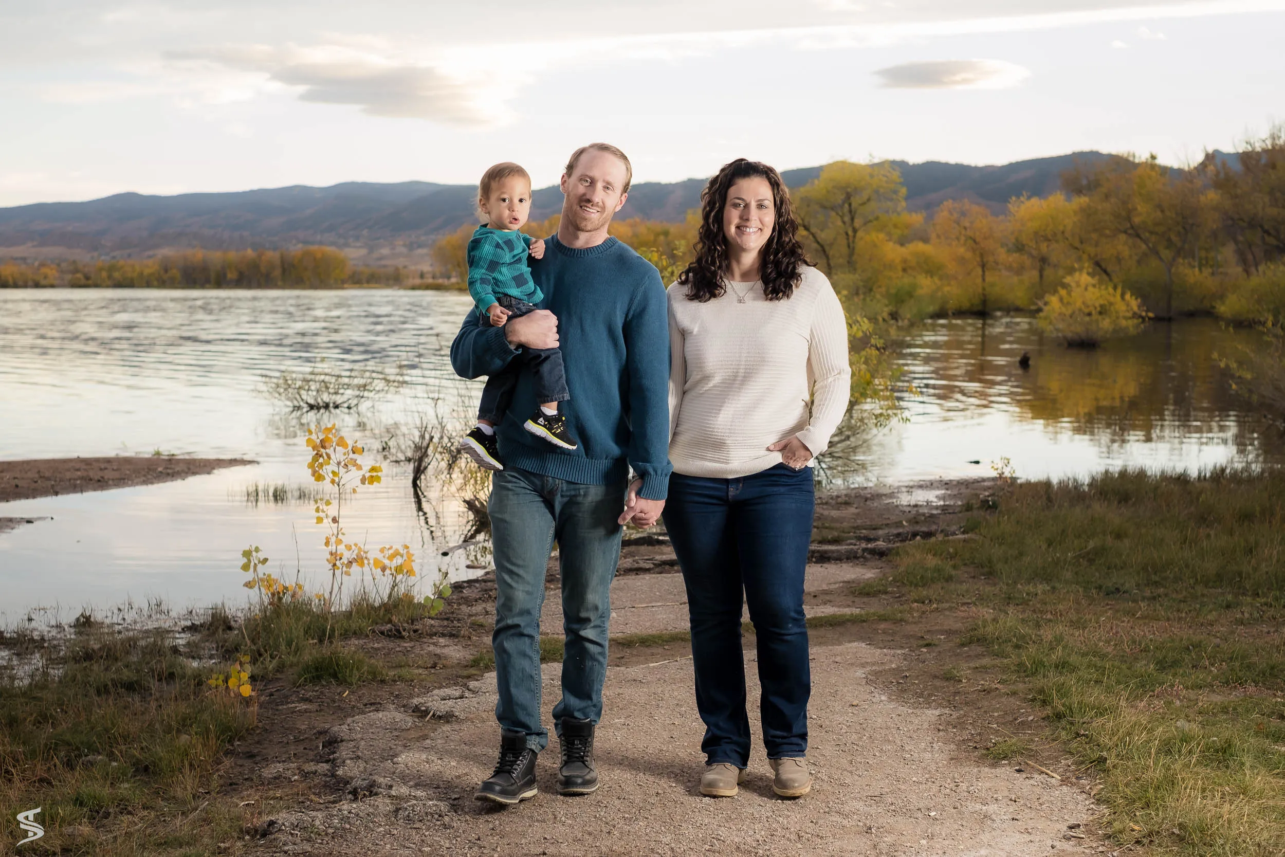 Parents holding hands beside a lake with their young child